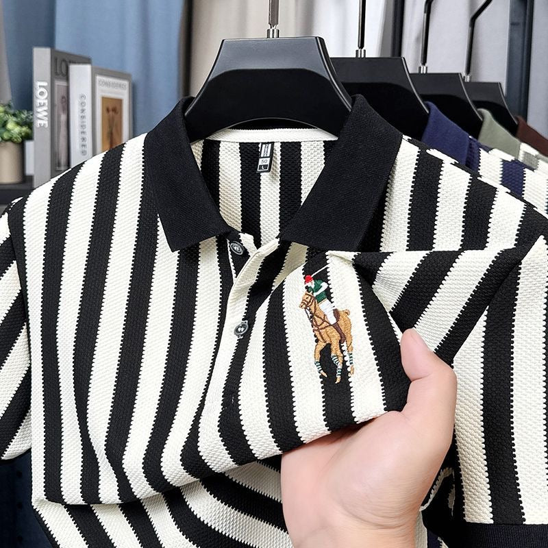 Black and white striped polo shirt with a brand logo held by a hand, hanging on a rack.